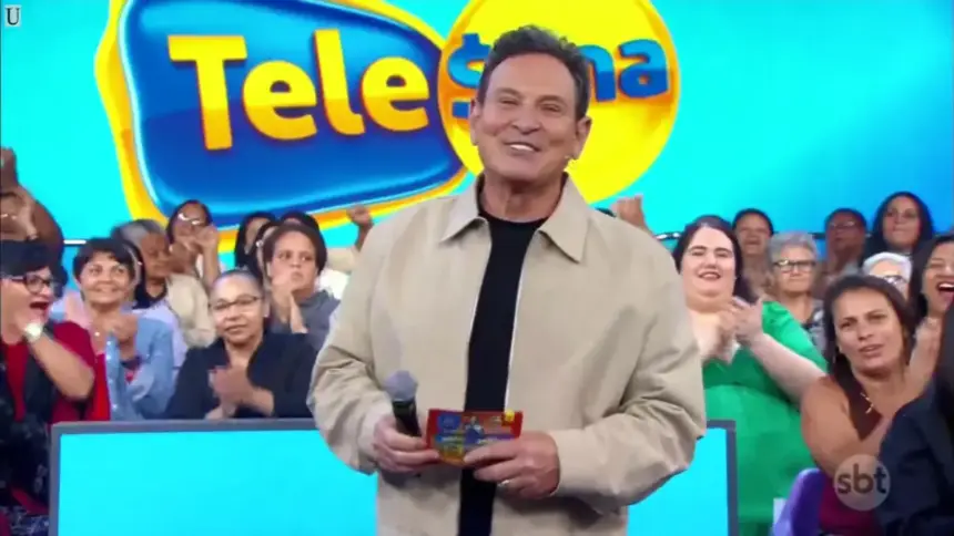 Luís Ricardo sorridente apresentando o sorteio da Tele Sena Semanal 79. Ele está em pé em frente a plateia