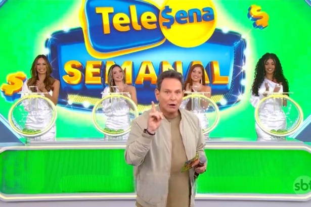 Luís Ricardo aponta para o alto e segura um bilhete da Tele Sena Semanal 77. O cenário está verde