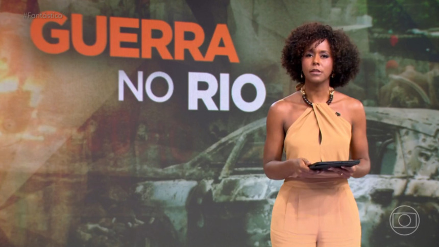 Maju Coutinho em pé no cenário, em trecho de edição do Fantástico, com o letreiro "Guerra no Rio" exposto no telão