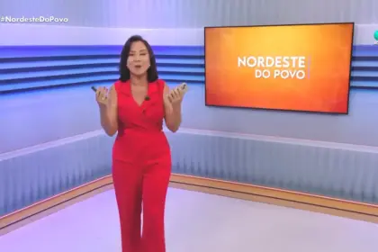 Katiuzia Rios de macacão vermelho no centro do cenário do Nordeste do Povo. Ao fundo paredes em tons de azul e branco, com uma tela de LED