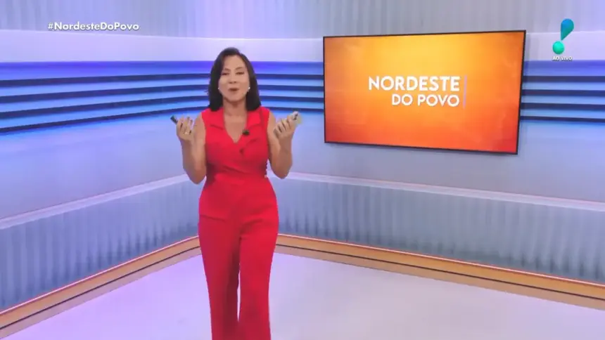 Katiuzia Rios de macacão vermelho no centro do cenário do Nordeste do Povo. Ao fundo paredes em tons de azul e branco, com uma tela de LED