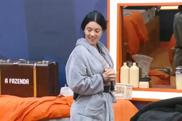 Rayane sorrindo e olhando para a mala ao lado da cama no quarto de A Fazenda 17 após presentear Yoná