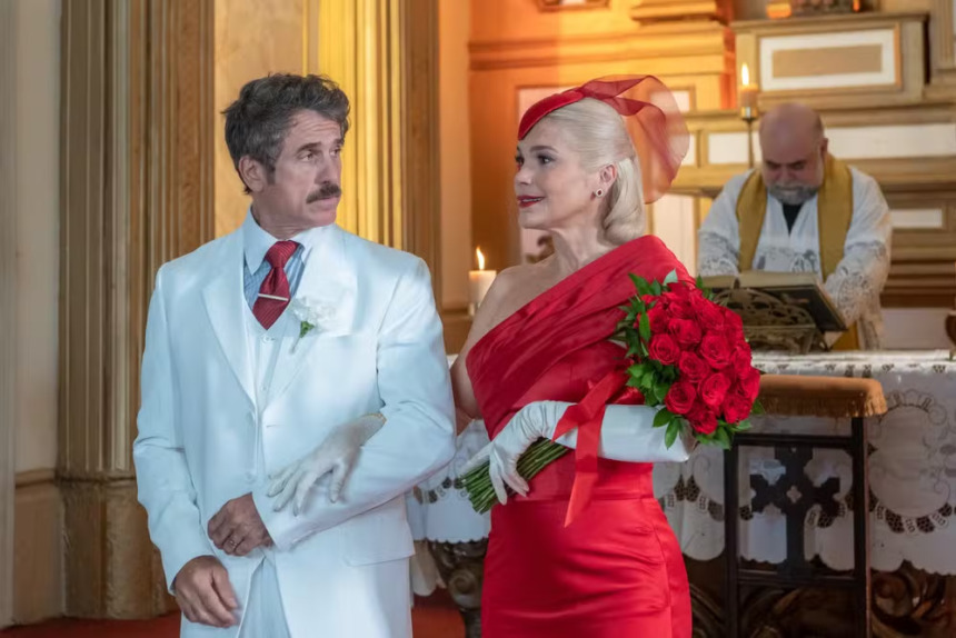 Ernesto olha para Sandra que sorrir com seu longo vestido vermelho em cena de Êta Mundo Melhor!