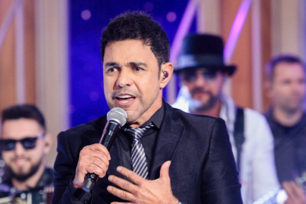Zezé Di Camargo com a mão no peito canta no palco do programa Sabadou no SBT