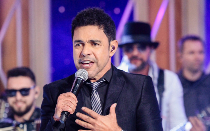 Zezé Di Camargo com a mão no peito canta no palco do programa Sabadou no SBT