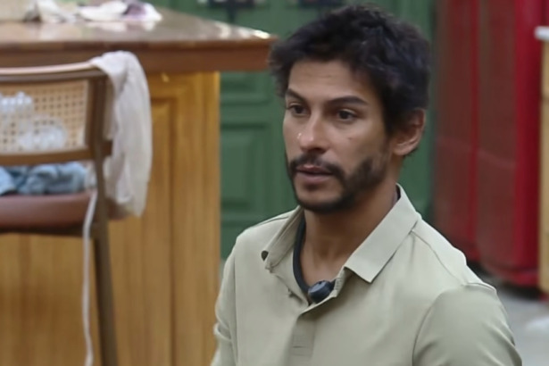 Shia, com feição de raiva, sentado no sofá da sala de A Fazenda
