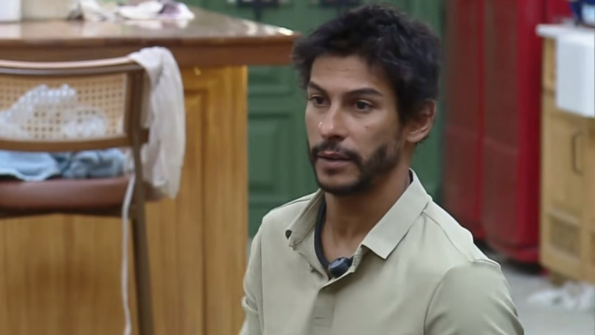 Shia, com feição de raiva, sentado no sofá da sala de A Fazenda