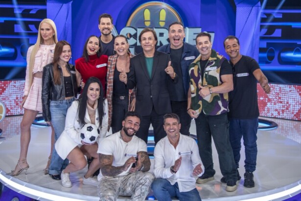 Tom Cavalcante e os 11 participantes famosos do programa de game show Acerte ou Caia, posando juntos no palco de luzes azuis