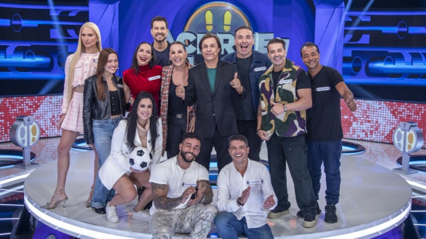 Tom Cavalcante e os 11 participantes famosos do programa de game show Acerte ou Caia, posando juntos no palco de luzes azuis