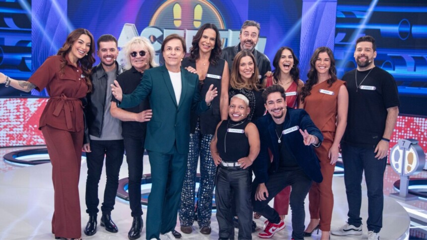 Tom Cavalcante e os 11 participantes famosos do programa de game show Acerte ou Caia, posando juntos no palco de luzes azuis