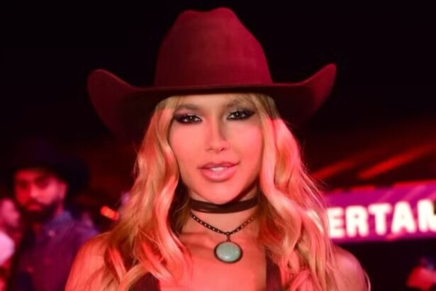 Influenciadora Virginia Fonseca em close-up, usando chapéu de cowboy vermelho e gargantilha, sorrindo em evento com luzes avermelhadas