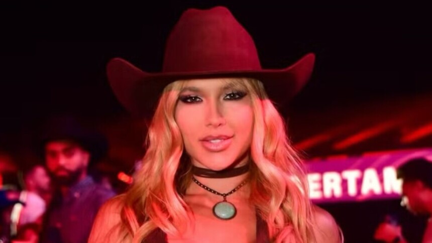 Influenciadora Virginia Fonseca em close-up, usando chapéu de cowboy vermelho e gargantilha, sorrindo em evento com luzes avermelhadas