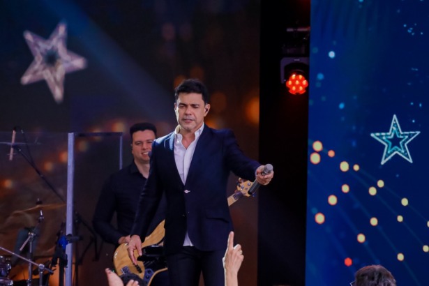 Zezé Di Camargo aponta o microfone para a plateia que assiste ao show especial de Natal no SBT