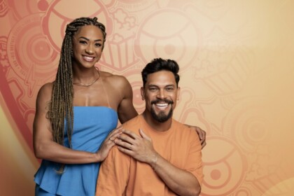 Aline de vestido azul ao lado de Vinicius Nascimento. Os dois estão sentados em frente a uma parede com decoração do BBB 26