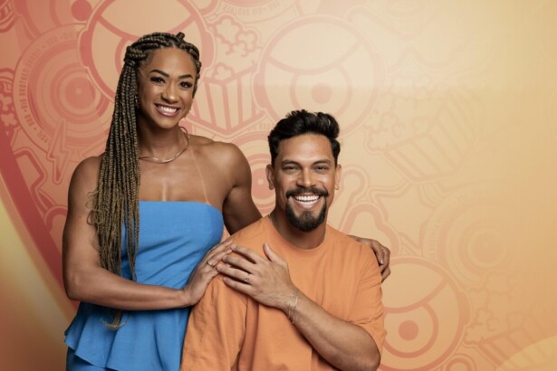 Aline de vestido azul ao lado de Vinicius Nascimento. Os dois estão sentados em frente a uma parede com decoração do BBB 26