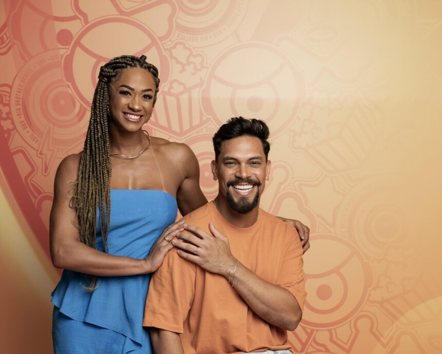 Aline de vestido azul ao lado de Vinicius Nascimento. Os dois estão sentados em frente a uma parede com decoração do BBB 26