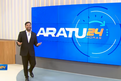 Alex Silvestre de terno escuro caminhando e sorrindo no cenário do Aratu 24 Horas