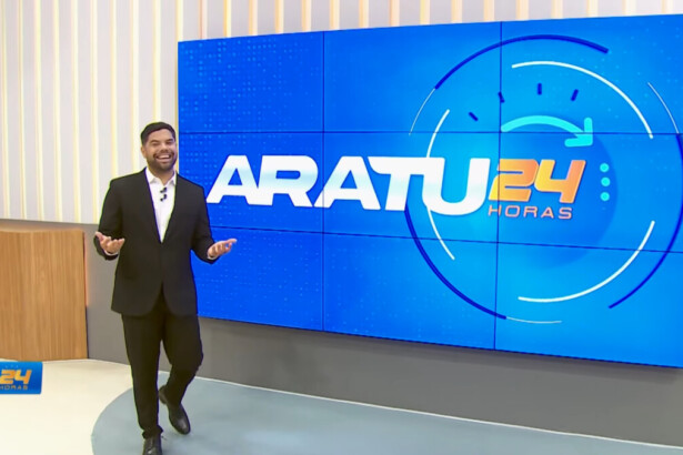 Alex Silvestre de terno escuro caminhando e sorrindo no cenário do Aratu 24 Horas