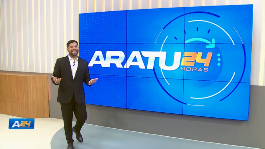 Alex Silvestre de terno escuro caminhando e sorrindo no cenário do Aratu 24 Horas