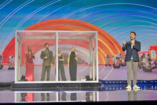 Tadeu Schmidt ao lado de uma mini casa de vidro com ex-participantes do BBB no palco do Upfront Globo 2026