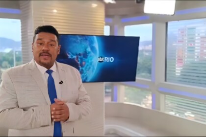Caio Álex de terno e em pé no cenário do SBT Rio 2ª Edição