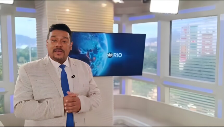 Caio Álex de terno e em pé no cenário do SBT Rio 2ª Edição