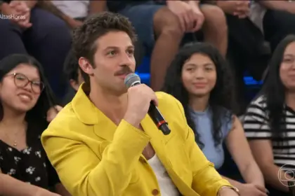 Chay Suede de blase amarelo sorrindo no cenário do Altas Horas onde falou sobre sua próxima novela das 9