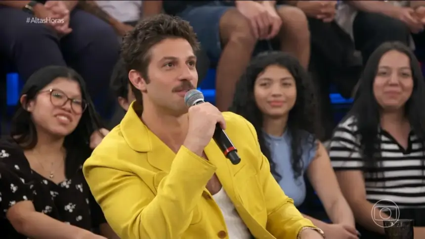 Chay Suede de blase amarelo sorrindo no cenário do Altas Horas onde falou sobre sua próxima novela das 9