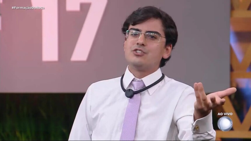 Dudu Camargo de gravata rosa e blusa branca no cenário da Formação da Roça de A Fazenda 17