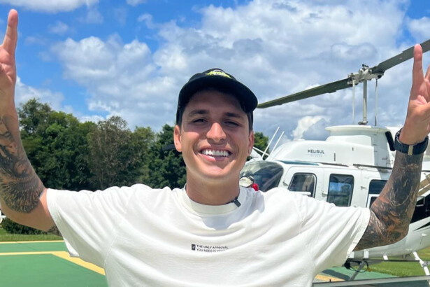 Felipe Prio faz sinal de vitória em frente a um helicóptero