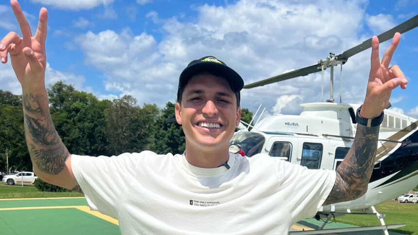 Felipe Prio faz sinal de vitória em frente a um helicóptero