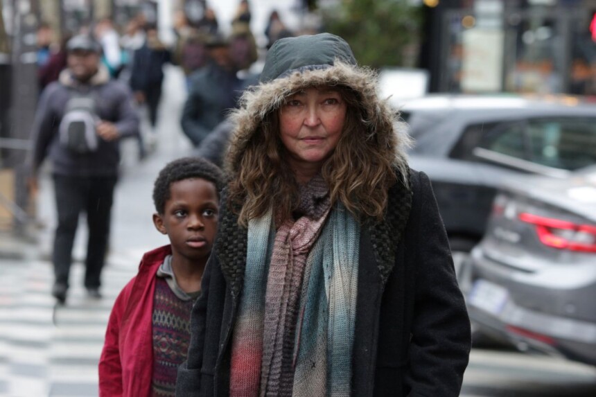 Mulher com roupa de frio caminha na frente de uma criança negra pelas ruas de Paris em cena do filme Sob as Escadas de Paris, da TV Aparecida