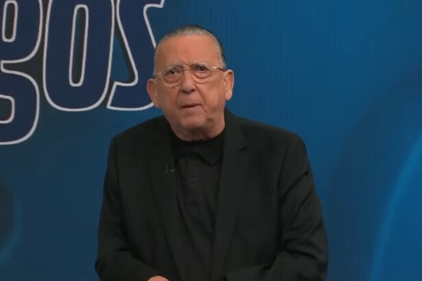 Galvão veste terno preto e camisa preta no cenário do programa Galvão e Amigos na Band