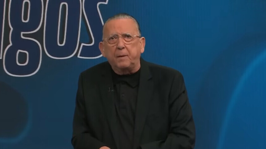 Galvão veste terno preto e camisa preta no cenário do programa Galvão e Amigos na Band