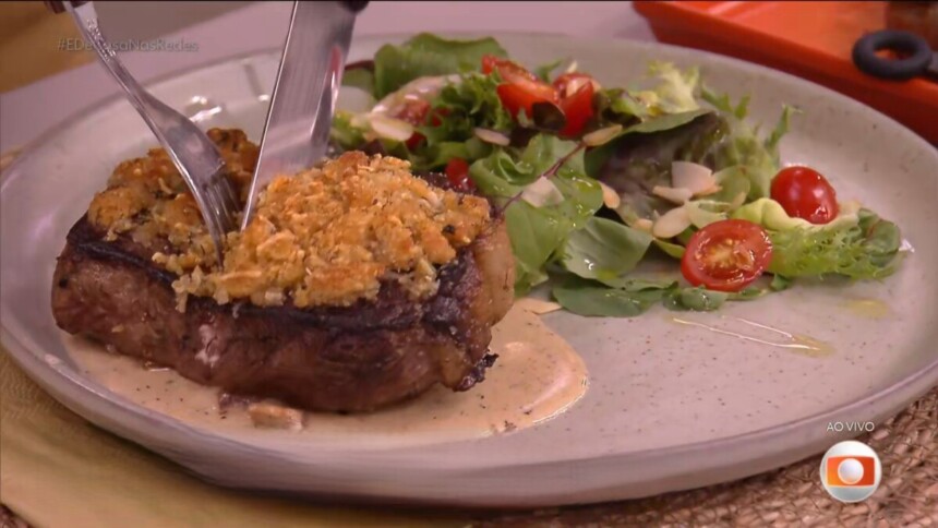 Bife de chorizo com crosta de ervas no prato branco do É de Casa, acompanhado de uma salada