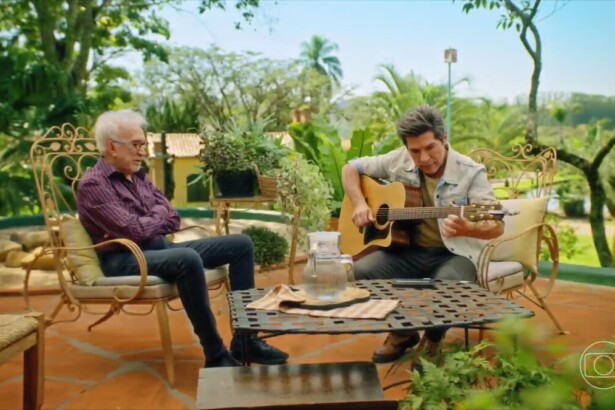 Moacyr Franco sentado em frente a Daniel que toca um violão durante gravação do Viver Sertanejo ao ar livre em uma fazenda