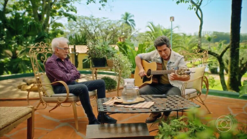 Moacyr Franco sentado em frente a Daniel que toca um violão durante gravação do Viver Sertanejo ao ar livre em uma fazenda