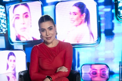 Naiara Azevedo de vestido vermelho no cenário do especial de fim de ano da RECORD. Ao fundo um telão com imagens da cantora