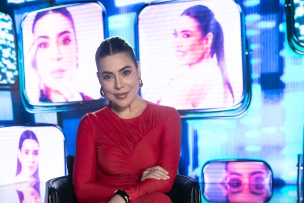 Naiara Azevedo de vestido vermelho no cenário do especial de fim de ano da RECORD. Ao fundo um telão com imagens da cantora
