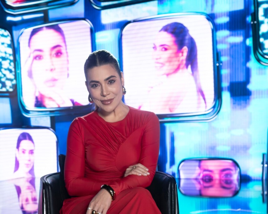 Naiara Azevedo de vestido vermelho no cenário do especial de fim de ano da RECORD. Ao fundo um telão com imagens da cantora