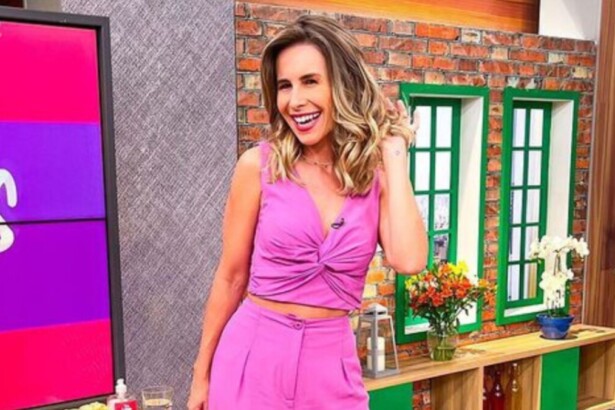 Pamela Domingues sorridente e passando a mãos no cabelo no cenário do programa Mulheres