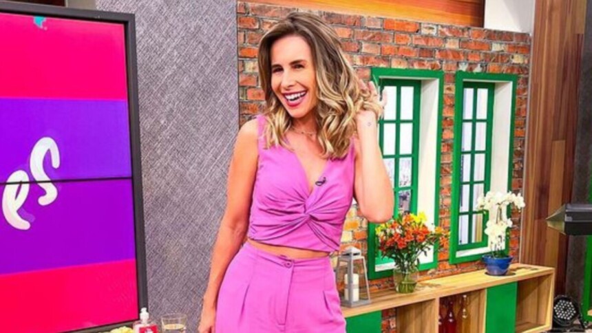 Pamela Domingues sorridente e passando a mãos no cabelo no cenário do programa Mulheres