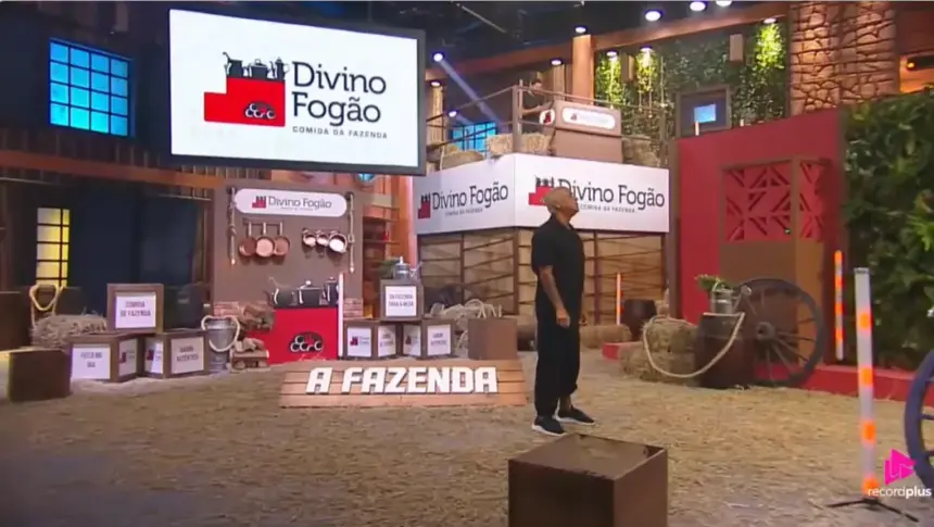 Telões com o logo do Divino Fogão no cenário da última Prova de A Fazenda 17. Walério em pé no centro do cenário
