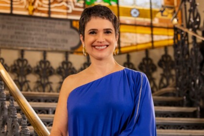 Sandra Annenberg sorrindo, de vestido azul, em frente uma escala, no cenário da Retrospectiva 2025