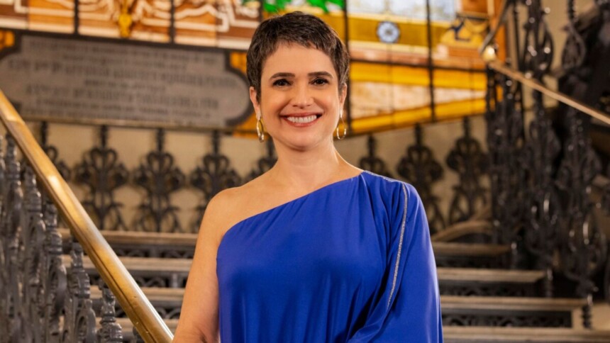 Sandra Annenberg sorrindo, de vestido azul, em frente uma escala, no cenário da Retrospectiva 2025