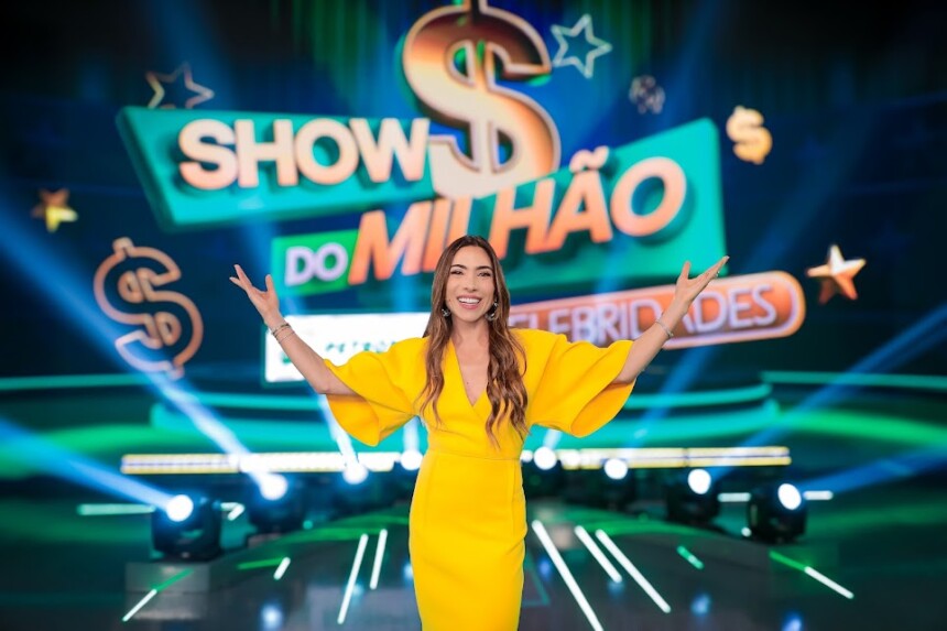 Patricia Abravanel abre os braços em frente ao telão com o logo do Show do Milhão