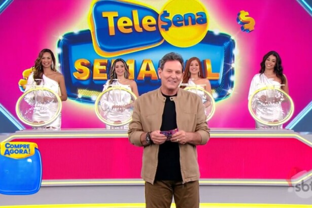 Luis Ricardo segura o bilhete da edição 81 da Tele Sena Semanal em frente aos globos dos sorteios, as assistentes e ao telão do cenário na cor rosa