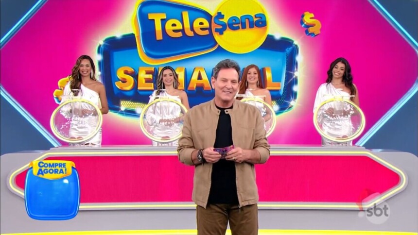 Luis Ricardo segura o bilhete da edição 81 da Tele Sena Semanal em frente aos globos dos sorteios, as assistentes e ao telão do cenário na cor rosa