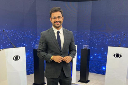 Tulio Amancio ao lado de bancada s com o logo da Band