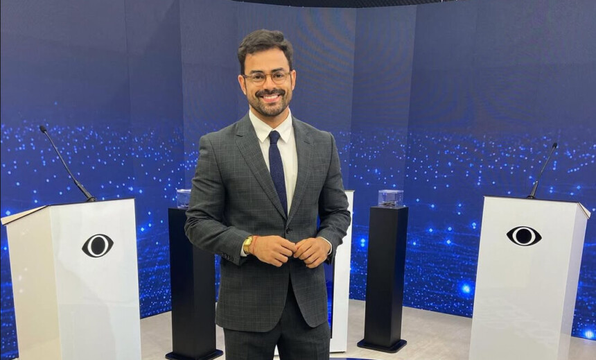 Tulio Amancio ao lado de bancada s com o logo da Band